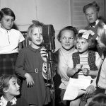 Barn som ska provsjunga inför ett radioprogram samlade runt en mikrofon