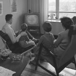 Två vuxna och två barn sitter i ett vardagsrum framför en tv-apparat