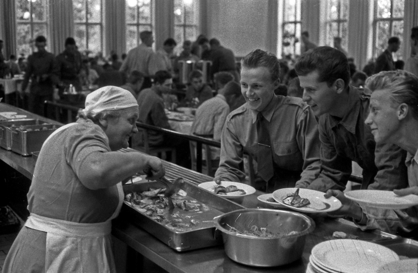 En kvinna serverar tre unga män surströmmin ur ett bleck