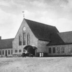 Bilden visar en järnvägsstation, en äldre byggnad med klocka på väggen.