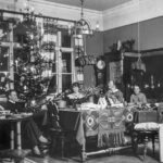 Bilden visar en familj som sitter vid ett bord. Ala är vuxna. I bakgrunden syns en julgran