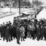 Bilden visar en grupp med män som står framför en rad med lastbilar. det är snö på marken.