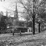 Bilden visar två barn som leker med de vissna löven invid Selångersån. I bakgrunden skymtar en kyrka och en bro.