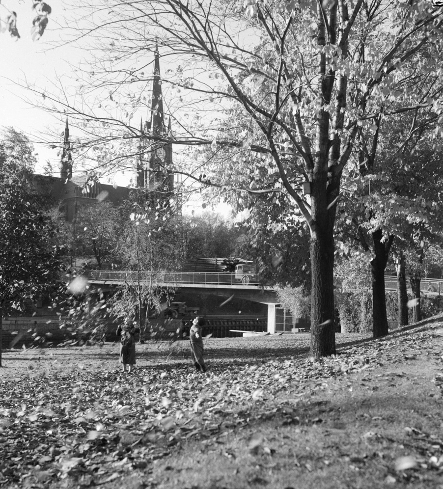 Bilden visar två barn som leker med de vissna löven invid Selångersån. I bakgrunden skymtar en kyrka och en bro.