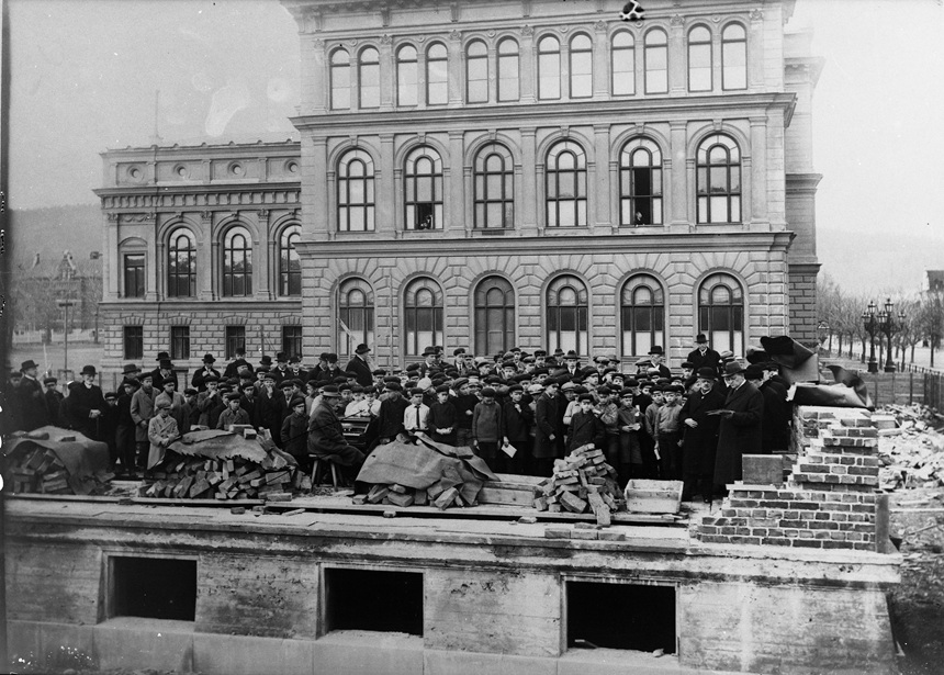 Bilden visar en byggarbetsplats 1925 med påbörjade murar och stor publik.